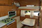 Interior photo shows the kitchen countertop, wood work and dining area in an old Aladdin travel trailer - model Genie