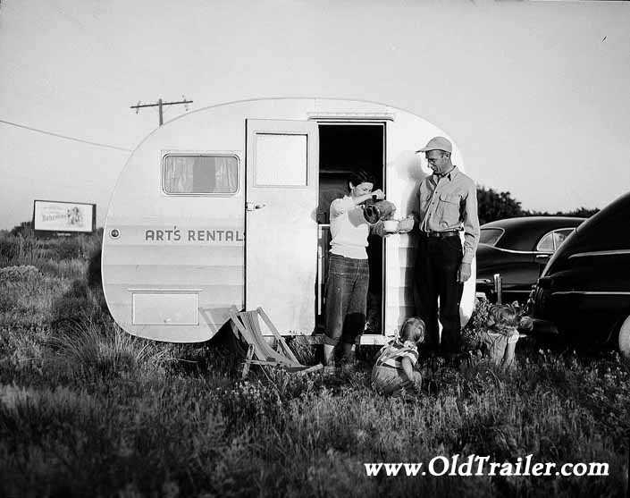 Government photo shows a young family with their 1940's vintage canned ham travel trailer, at the Hanford Trailer Camp in Washington