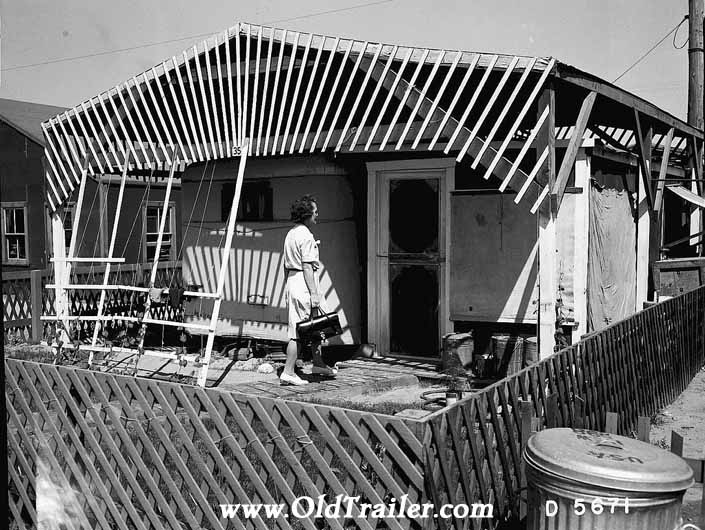Government photo shows a woman visiting a family's home next to their 1940's vintage trailer, at the Hanford Trailer Camp in Washington