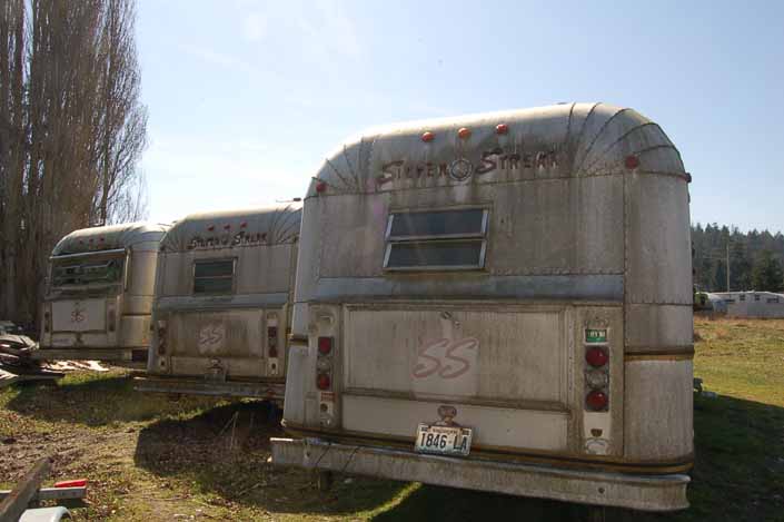 Vintage trailer junkyard has a row of Silver Streak trailers with the standard Silver Streak large rear bumper