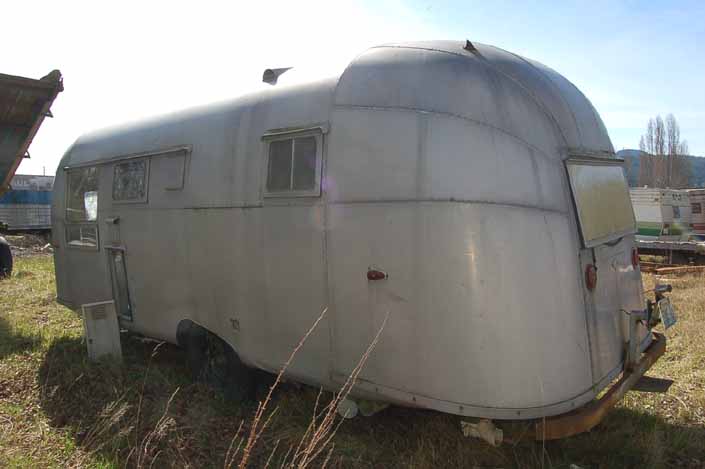 Vintage trailer junkyard has a vintage silver-bullet aluminum travel trailer ready for restoration