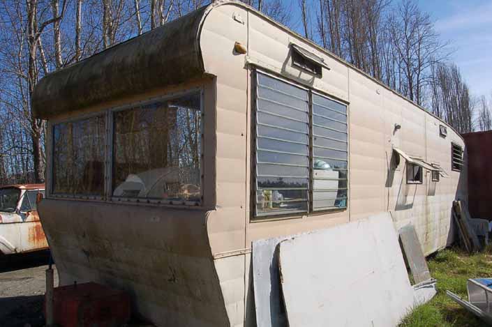 Vintage trailer junkyard has a vintage travel trailer with surface moss but ready for restoration