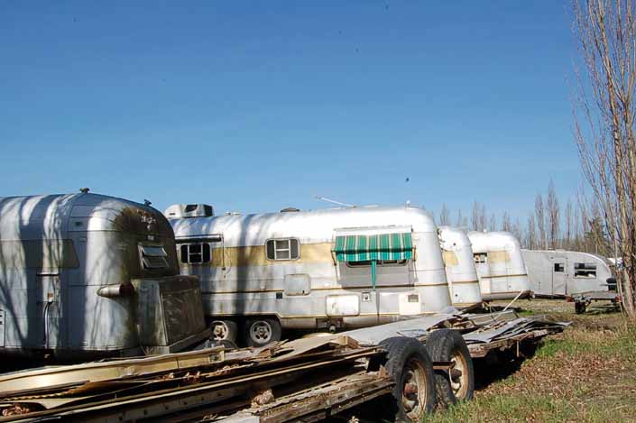 Vintage trailer junk yard has a torn-down vintage trailer twin-axle frame with wood floor platform