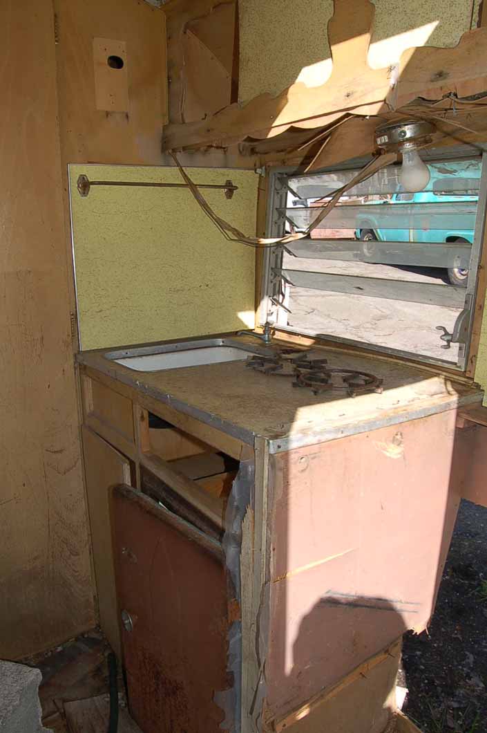 Project Shasta Compact trailer parked in a vintage trailer Storage Yard has a damaged kitchen counter top and cabinet