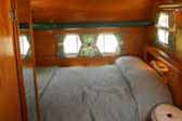 Inviting bedroom with beautifully refinished woodwork in a 1955 Aljoa Sportsman vintage trailer