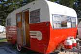 Restored 1955 Aljoa travel trailer with propane tanks painted red and white to match the trailer