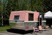 Photo shows rear view of beautifully restored pink and white 1961 Holiday House vintage trailer