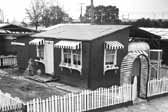 Old photo shows a young girl watering the garden outside family home next to their 1940's vintage trailer, at the Hanford Trailer Camp in Washington