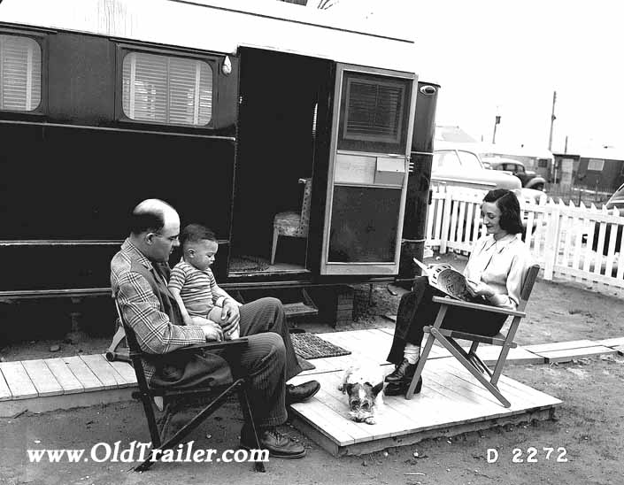 Government photo shows a family and their dog, sitting outside their 1940's vintage trailer, at the Hanford Trailer Camp in Washington