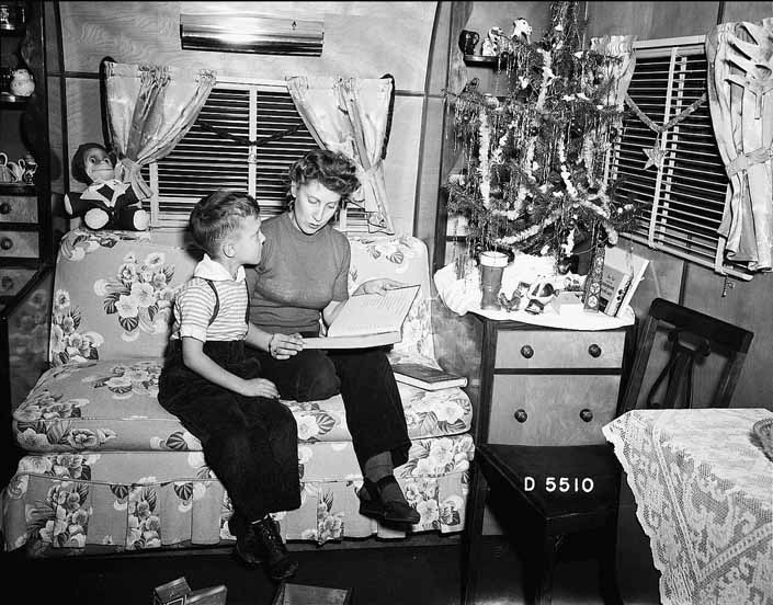 Government photo shows a mother reading to her son next to the Christmas tree in a vintage trailer, at the Project Hanford Trailer City in Washington