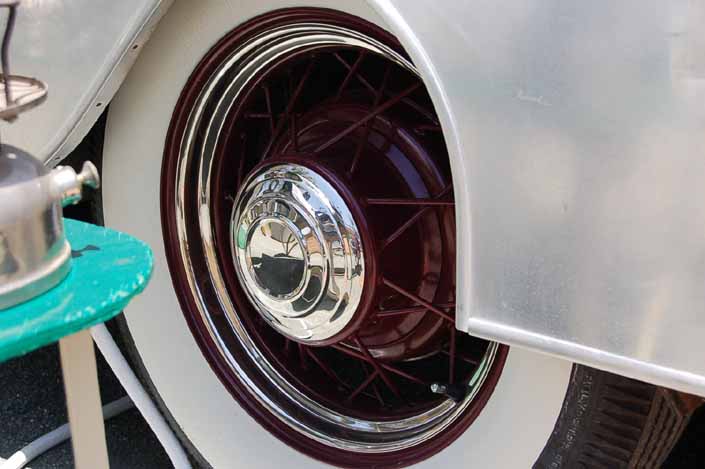 This image shows an example of vintage trailer wire wheels painted maroon, with small chrome hubcaps and beauty rings