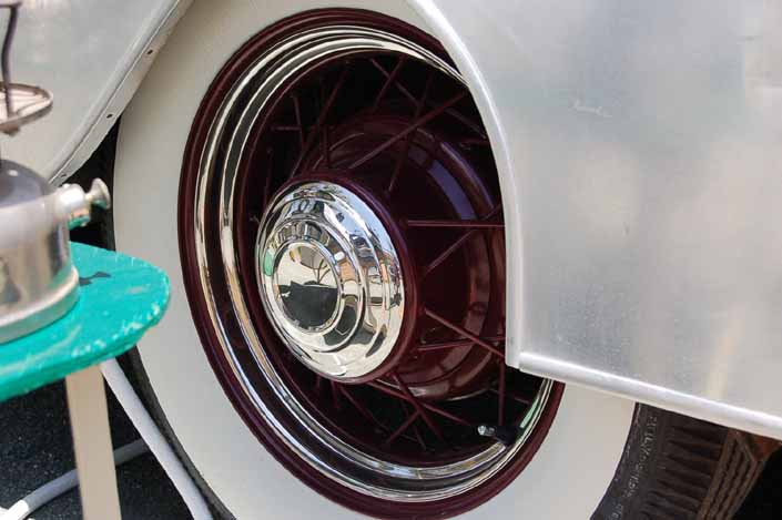 This image shows an example of vintage trailer wire wheels painted maroon, with small chrome hubcaps and beauty rings