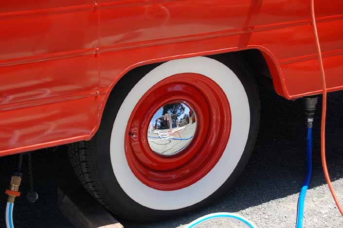 Photo shows an example of a vintage trailer with wheels painted orange, small baby moon hubcaps and wide whitewall tires
