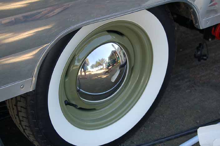 Photo shows an example of a vintage trailer with wheels painted olive green and with bay moon hubcaps and wide whitewall tires