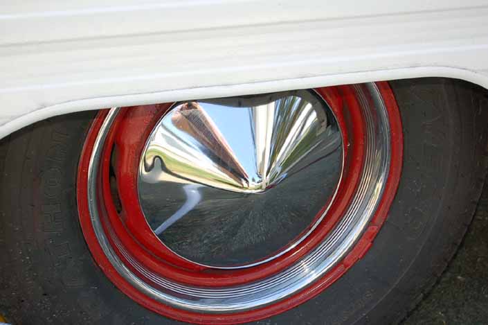Image is an example of a vintage trailer wheel painted red and with a pointy chrome hubcap and beauty ring