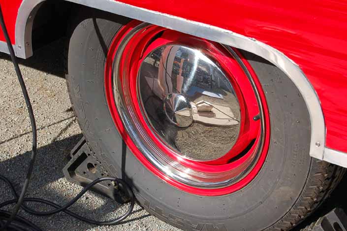 Photo shows an example of a vintage trailer with wheels painted red, with chrome hubcaps and beauty rings