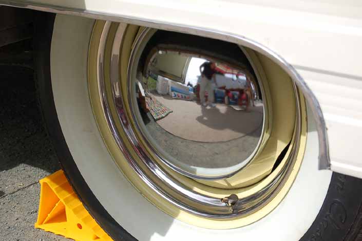 Nice example of a vintage trailer wheel painted light yellow, and with a chrome beauty ring and hubcap and wide whitewall tires