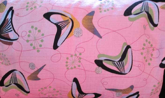 This photo shows a swatch of retro fabric with a Googie boomerangs design on a pink background, for your vintage trailer