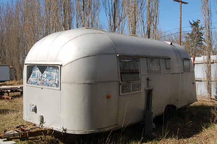 Vintage trailer junk yard has a restorable vintage aircraft-styled aluminum trailer in storage