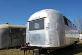 Classic Airstream trailer with dents is parked in a vintage trailer storage yard