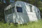 Original Shasta Airflyte trailer parked in the weeds in a vintage trailer storage yard
